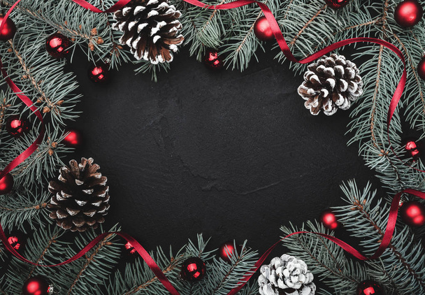 Fond en pierre noire avec un cadre de branches de sapin décorées de boules et ruban rouge. Cônes de pin. Vue de dessus. Avec espace texte
 - Photo, image