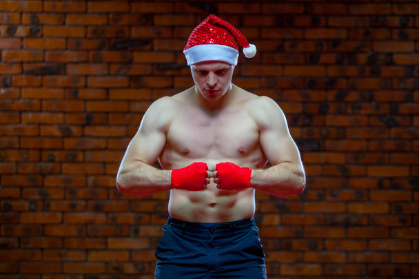Christmas. Muscular Fighter kickbox boxing Santa Claus With Red Bandages the background of a brick wall. - Φωτογραφία, εικόνα