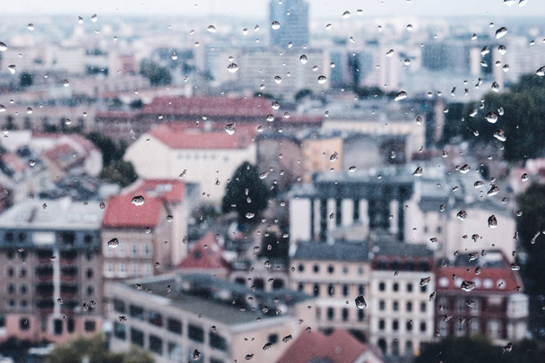 Raindrops on the dirty glass, behind the glass blurred panorama of old colored city, abstract retro nostalgically background - Photo, Image
