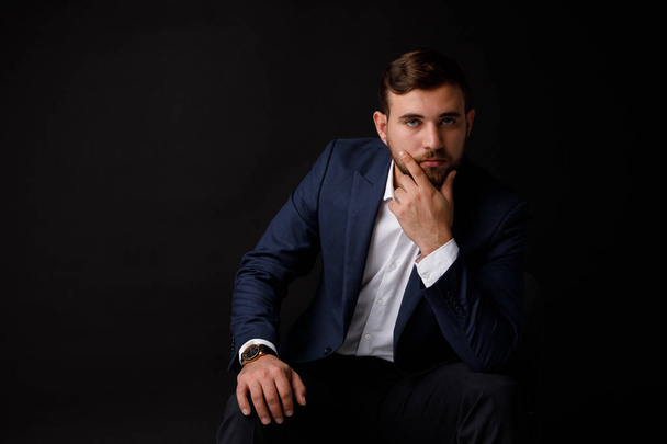 Close-up portrait of a young and serious businessman with a beard in a formalwear on a black background. The concept of a success. - Foto, Bild