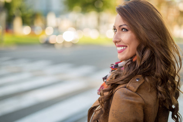 Beautiful young woman smiling while waiting at a cross walk at daytime - Zdjęcie, obraz
