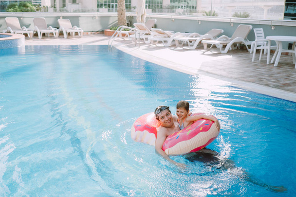 vader met daughater duik met opblaasbare donut in het zwembad - Foto, afbeelding
