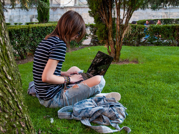Üniversite Kampüsü bir üniversitede bir parkta çim üzerinde oturan bir dizüstü bilgisayar ile okuyan bir genç kadın - Fotoğraf, Görsel