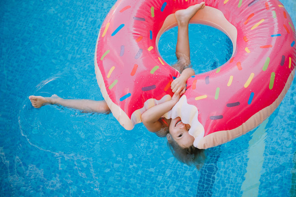 Kislány, úszás a medencében felfújható fánk - Fotó, kép