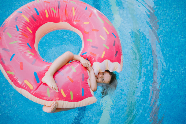 Menina nadando com donut inflável na piscina
 - Foto, Imagem