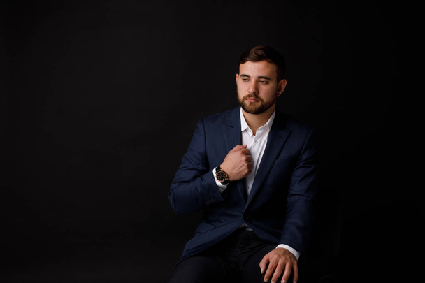Close-up portrait of a young and thoughtful businessman with a beard in a suit on a black background. The concept of a successful worker. - Photo, image