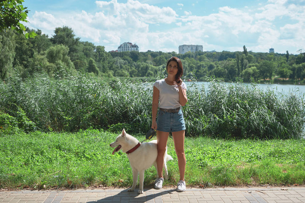 Mujer joven y bonita paseando al aire libre con su adorable perro husky en un parque. Hermosa chica divirtiéndose con su linda mascota
. - Foto, Imagen