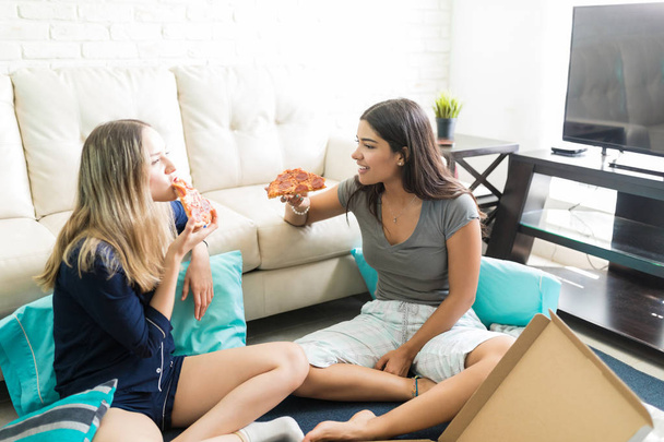 Amigas interactuando mientras disfrutan de la pizza en la sala de estar en casa
 - Foto, imagen