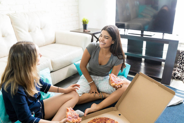 Young females having pizza while enjoying pajama party in living room - Фото, зображення