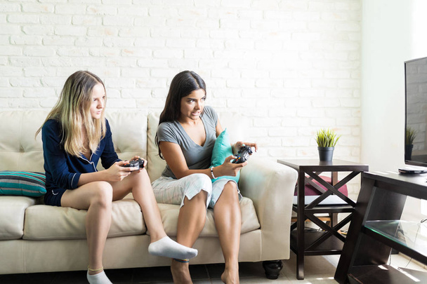 家でゲームをプレイしながら互いに競合する多民族の女性の友人 - 写真・画像