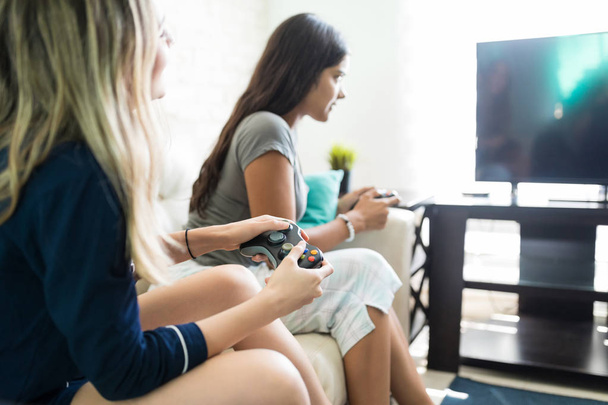 若い女性が友人の家でぶらぶらしながらビデオゲーム コンソールを用いた - 写真・画像