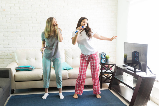 Fiatal női szobatársak, éneklés és a tánc közben karaoke party otthon - Fotó, kép
