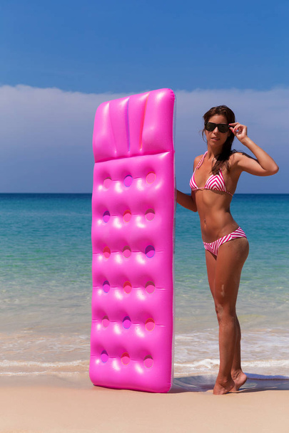 Young slim brunette woman in sunglasses gets suntan with an air mattress on the tropic beach - Фото, зображення