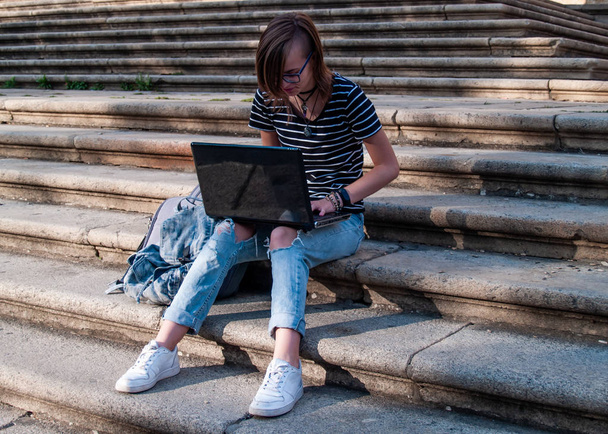 Una adolescente que estudia con un portátil en las escaleras de una universidad en un campus universitario
 - Foto, imagen