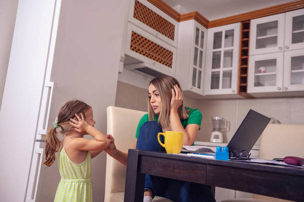 umtriebige Mutter von zu Hause, die mit dem Computer arbeitet, während sie sich um ihre Tochter kümmert - Foto, Bild