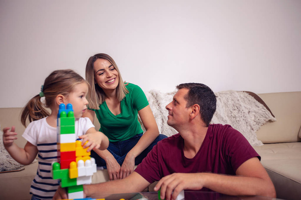 Happy family - smiling mother and father playing with cute daughter cubes together at home - Photo, Image
