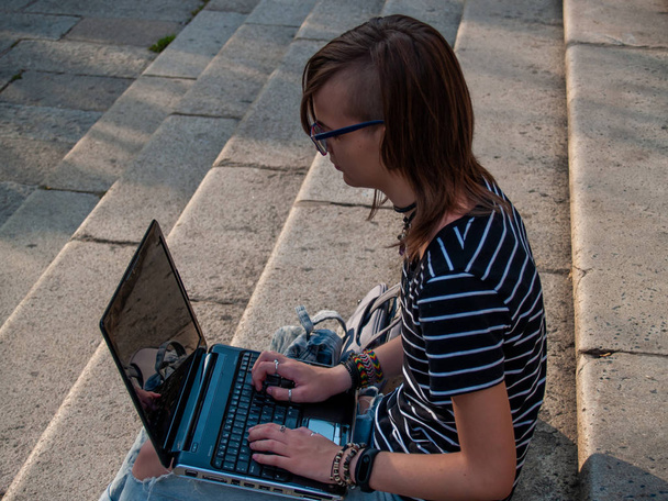 Μια Έφηβη γυναίκα μελετώντας με ένα φορητό υπολογιστή στα σκαλιά του Πανεπιστημίου της πανεπιστημιούπολης - Φωτογραφία, εικόνα