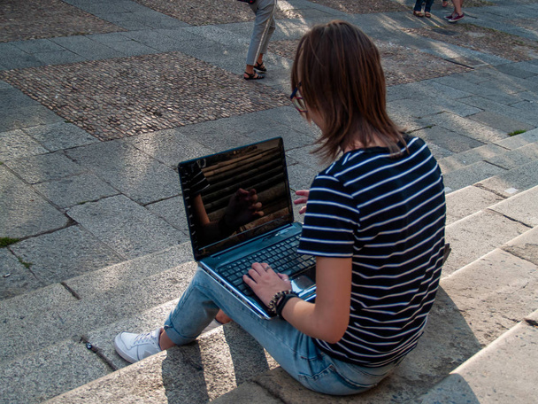 Bir üniversitede bir üniversite kampüsü merdiven üstünde a laptop ile okuyan bir genç kadın - Fotoğraf, Görsel