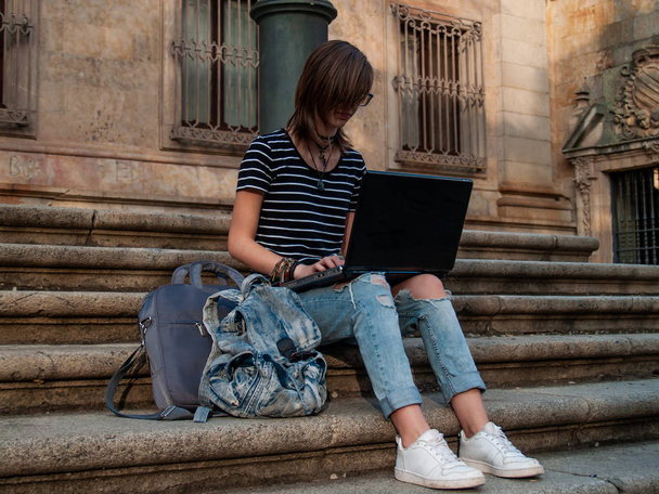 Uma adolescente estudando com um laptop nas escadas de uma universidade em um campus universitário
 - Foto, Imagem