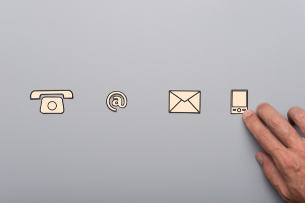 Business customer service concept - male hand placing paper cut communication icons in line on grey background. - Fotó, kép