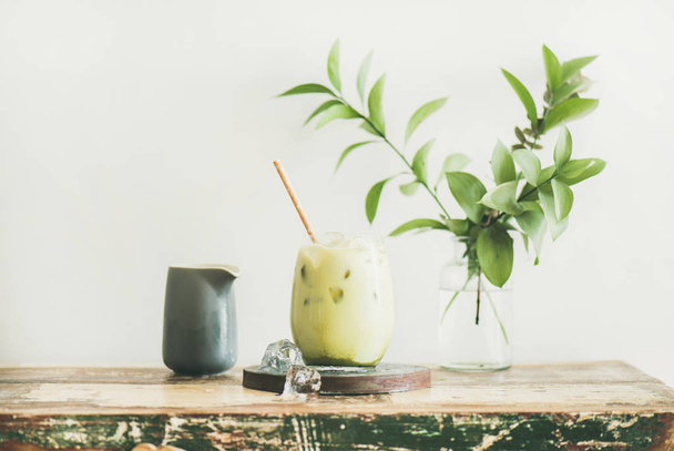 Iced matcha latte drink in glass, white wall and plant branches at background - Valokuva, kuva