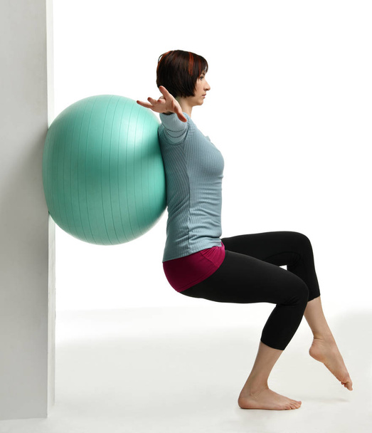 Female fitness instructor holds legs in gym and workout exercises for abdominals with green sport ball over white - Fotó, kép