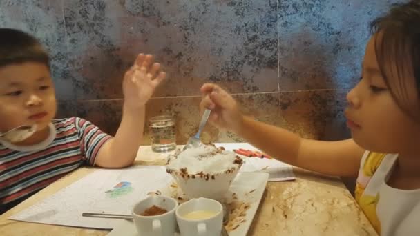 Lindo una niña y asiático un chico están comiendo helado en el restaurante
. - Metraje, vídeo
