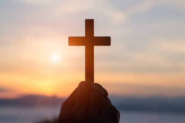 Силуэт от рук держа деревянный крест на фоне восхода солнца, Распятие, символ веры. - Фото, изображение