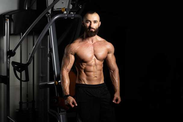 Young Man Standing Strong In The Gym And Flexing Muscles - Muscular Athletic Bodybuilder Fitness Model Posing After Exercises - Φωτογραφία, εικόνα