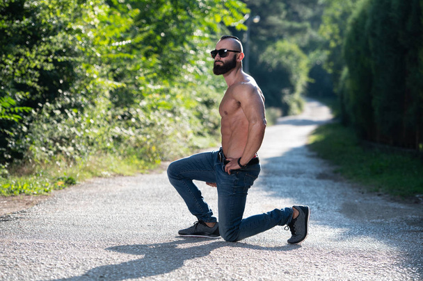 Handsome Young Model Kneeling Strong Outdoors and Flexing Muscles - Muscular Athletic Bodybuilder Man Posing - Φωτογραφία, εικόνα