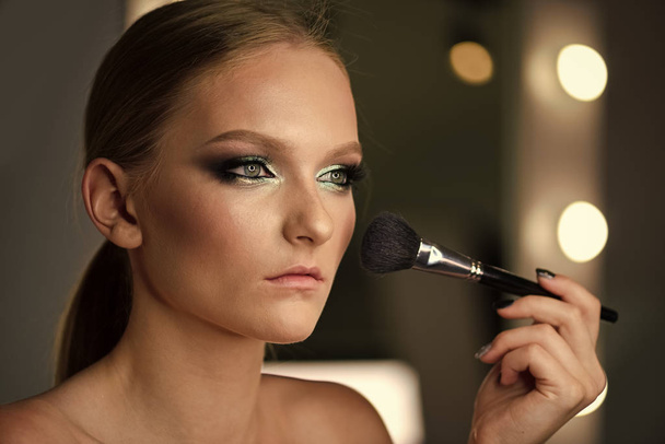 Beautiful teenage girl applying cosmetic powder on face with tassel, skin care concept - Fotó, kép