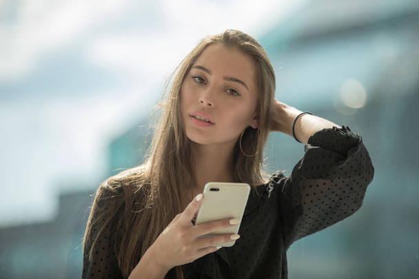 Attractive woman is sitting on the windowsill and uses a smartphone. - Foto, Imagem