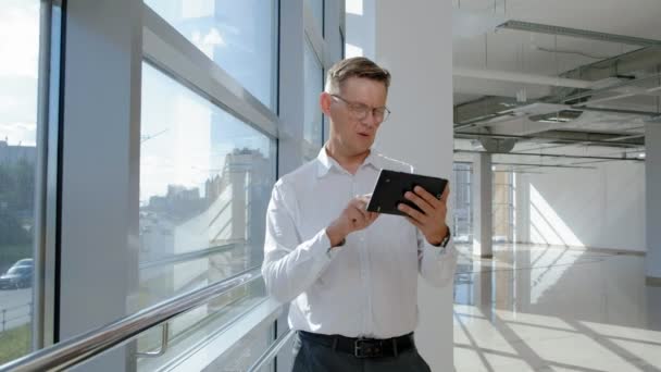 Mature businessman at a window with a tablet - Felvétel, videó