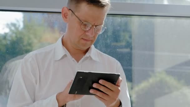 Mature businessman at a window with a tablet - Séquence, vidéo