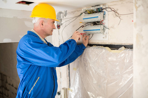 Senior electrotechnician connecting wiring system and completing the preparation of the electrical circuit home network - Foto, immagini
