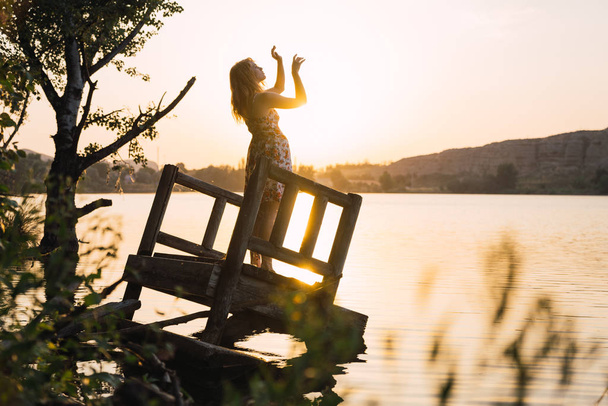 Frau steht im Sonnenlicht auf versunkenem Steg am See - Foto, Bild