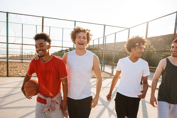 Portrait of four sporty men basketball players walking along playground outdoor during summer sunny day - Fotoğraf, Görsel