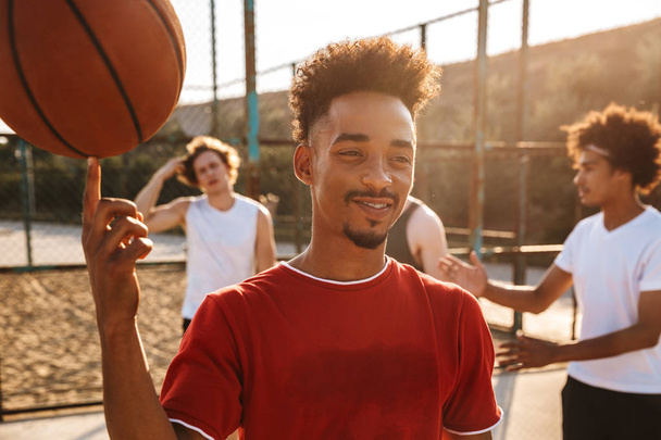 Portrait of young sporty men playing basketball at the playground outdoor and american guy spinning ball on his finger - Fotó, kép