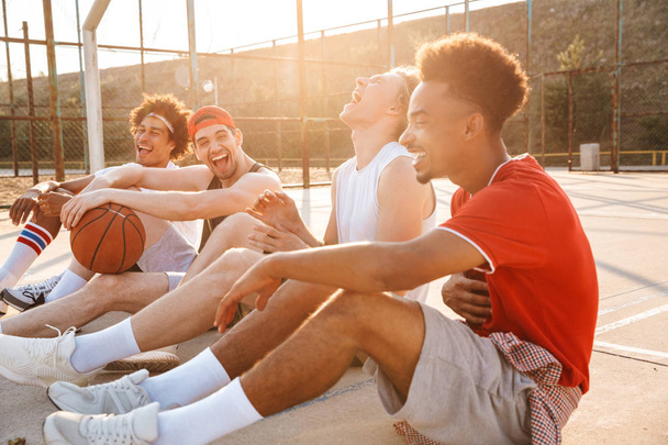 Group of laughing multiethnic friends basketball players sitting at the sports ground, talking - Foto, immagini