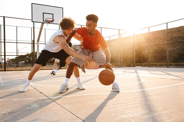 Group of young sporty multiethnic men basketball players playing basketball at the sport ground - Foto, Imagen