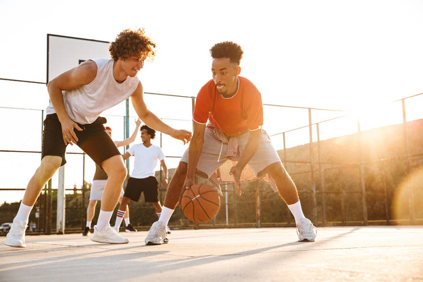 Group of young cheerful multiethnic men basketball players playing basketball at the sport ground - Foto, Imagen