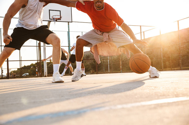 Cropped image of young multiethnic men basketball players playing basketball at the sport ground - Foto, afbeelding
