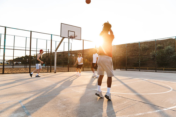 Group of young cheerful multiethnic men basketball players playing basketball at the sport ground - Photo, Image