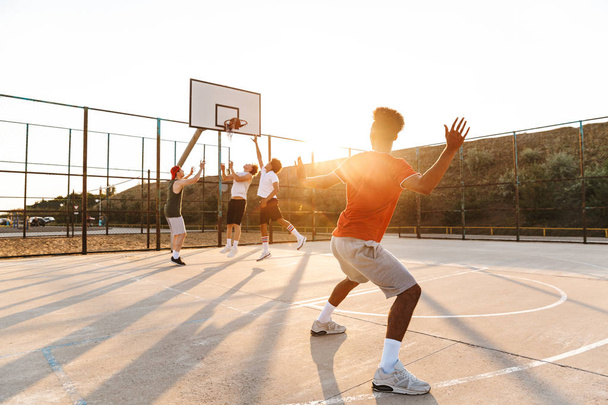 Group of young excited multiethnic men basketball players playing basketball at the sport ground - Foto, immagini