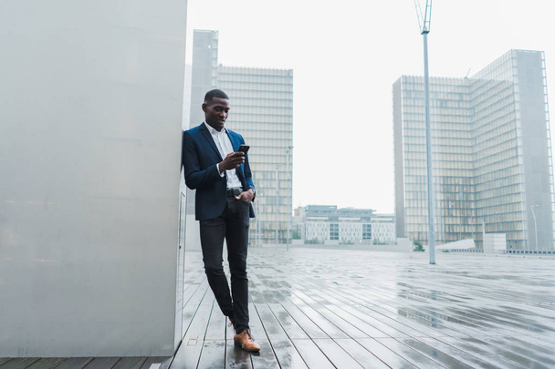 African American businessman using smartphone while standing in modern city - Photo, Image