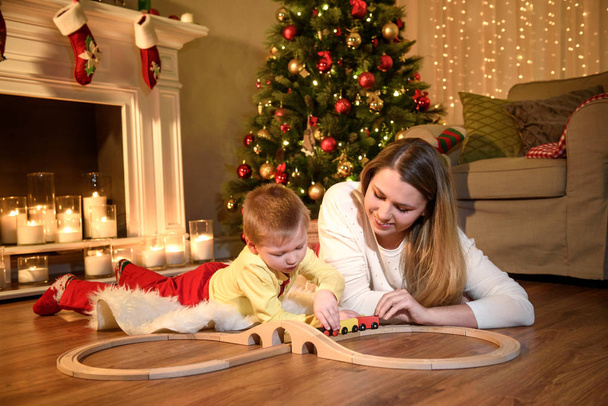 Beautiful moments of mom and son playing with a toy train. New Year's holidays. Toddler with mom in the festively decorated room with Christmas tree - Photo, Image