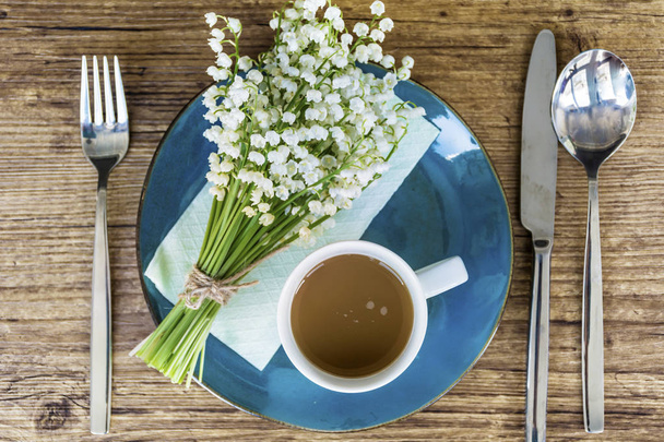 Spring Table Setting with Vintage Blue Cutlery and Lily of the Valley Flowers on a Wooden Background.Floral Table Decor with Coffee Cup.Top view - Foto, afbeelding