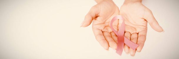 Two hands showing pink ribbon against breast cancer against white background - 写真・画像
