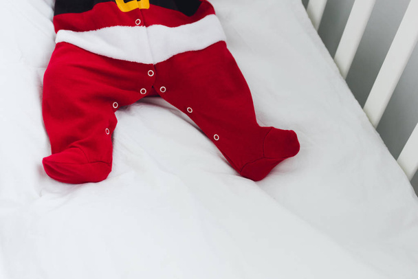 recortado disparo de pequeño bebé en traje de santa acostado en cama infantil
 - Foto, Imagen