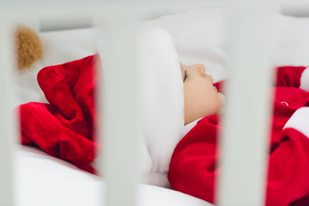 primer plano de bebé en traje de santa acostado en cama infantil
 - Foto, Imagen